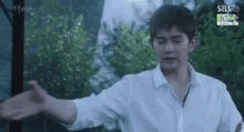 a man in a white shirt is standing with his arms outstretched in front of a tree .