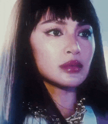 a close up of a woman 's face with long hair and a necklace .