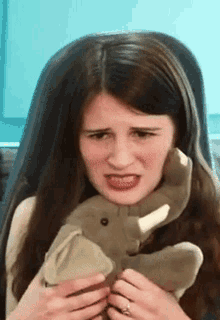 a woman is holding an elephant stuffed animal and making a face