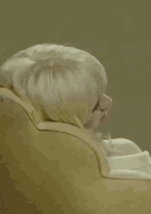 a woman with blonde hair is sitting on a yellow couch making a funny face .