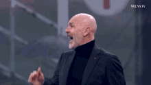 a man in a suit and black turtleneck is screaming in front of a milan tv sign