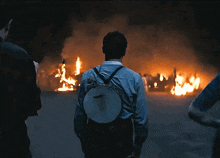 a man with a banjo on his back is looking at a fire
