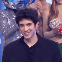 a man in a black shirt is smiling in front of a crowd of people .