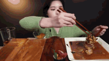 a woman is holding chopsticks over a plate of food on a wooden table