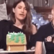 a woman in a black shirt is holding a small cake with green frosting .