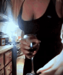 a woman in a black tank top is holding a wine glass