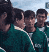 a group of men wearing green jackets with the number 001 on them are standing in a line .