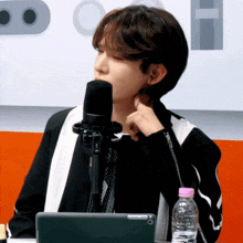 a young man is sitting in front of a microphone with a bottle of water next to him