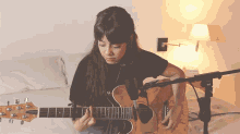 a woman is playing a guitar in front of a microphone and a lamp