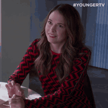 a woman in a red and black sweater sits at a table with her hands folded in front of a youngertv logo
