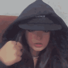 a woman wearing a black hoodie and a black hat is sitting on a couch .