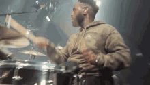 a man in a camo hoodie is playing drums on a stage