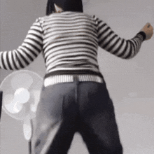 a woman in a black and white striped shirt is dancing in front of a fan