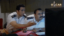 two men are looking at a computer screen that says oscar on the bottom