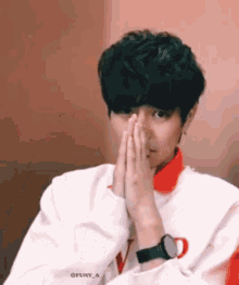 a young man wearing a watch is covering his face with his hands .