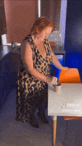a woman in a leopard print dress is standing next to a table with a cup of coffee on it .