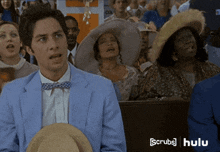 a man in a blue suit and bow tie is holding a hat in front of a crowd of people with hulu written on the bottom