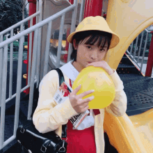 a girl wearing a yellow hat blows up a yellow balloon while holding a book that says oldies