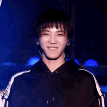 a young man wearing headphones and a black hoodie is smiling and clapping his hands .