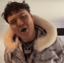 a man wearing a jacket with a fur collar is singing