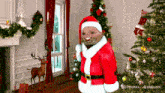 a man dressed as santa claus stands in front of a christmas tree in a living room