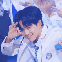 a young man in a white jacket and tie is making a peace sign with his hands .