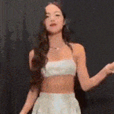 a woman in a white crop top and a white skirt is dancing on a stage .