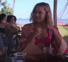 a woman in a pink top is sitting at a table with plastic cups
