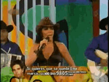 a woman in a cowboy hat is singing into a microphone with a sign that says si quieres que se quede emir