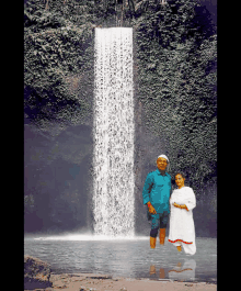 a man and a woman are standing in front of a waterfall
