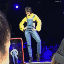 a woman in overalls is standing on a stage with her hands on her hips while a phone records her