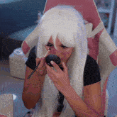 a woman in a white wig is applying makeup in front of a pink chair