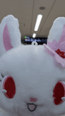a white stuffed animal with red eyes and a pink bow on its head