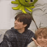 two men are sitting next to each other on a couch with a green octopus balloon .