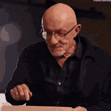 a bald man wearing glasses and a black shirt is holding a cardboard box