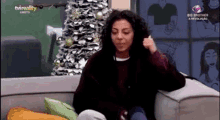 a woman is sitting on a couch with a christmas tree in the background and giving a thumbs up .