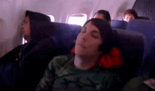a man is sleeping on an airplane with a red pillow around his neck
