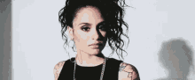 a woman with curly hair and a tattoo on her arm is wearing a black tank top and hoop earrings .