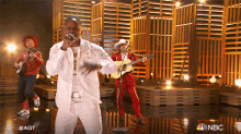 a man in a white suit is singing into a microphone on stage