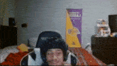 a man wearing headphones and a hat is sitting in a gaming chair in front of a lakers banner .