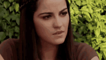 a woman with long dark hair is sitting in front of a bush .