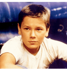 a young boy wearing a white t-shirt looks at the camera