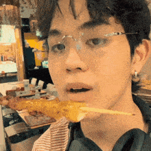 a young man wearing glasses is eating a piece of food on a stick