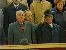 a man wearing a hat salutes while standing in a crowd
