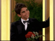a young boy wearing a tuxedo and bow tie is holding a bouquet of roses .