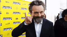 a man with a beard is giving the middle finger in front of a yellow sign that says sxswl