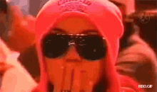 a woman wearing sunglasses and a pink hat covering her face with her hand