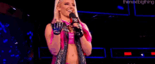 a woman with pink hair is holding a microphone on a stage .