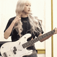 a woman with blonde hair is holding a white bass guitar with the letters zzm on the neck