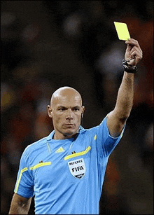 a soccer referee is holding a yellow card in his hand .